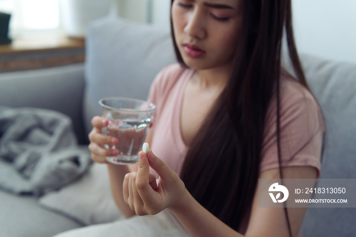 Young Asian girl having headache and high temperature from illness holding pill of medicine and wate