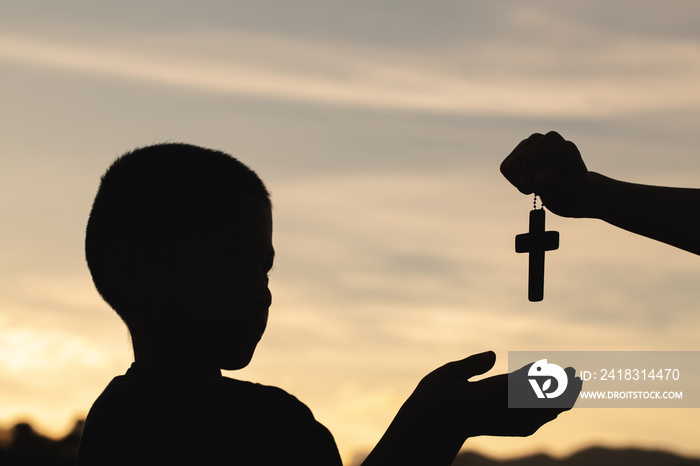 Silhouette of a man praying with a cross in hand at sunrise,  religion concept.