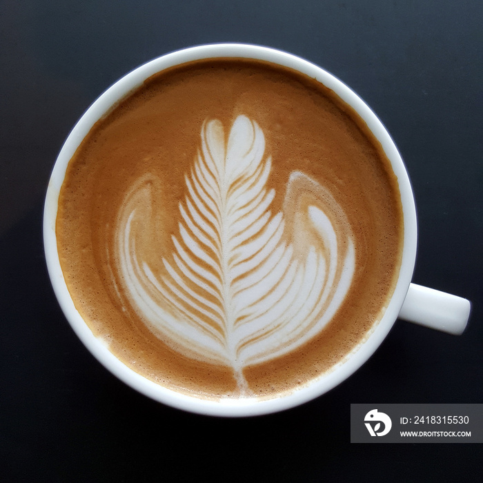 Top view of a mug of latte art coffee on black background.