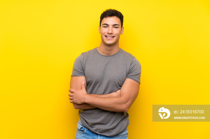 Handsome man over isolated yellow wall keeping the arms crossed in frontal position