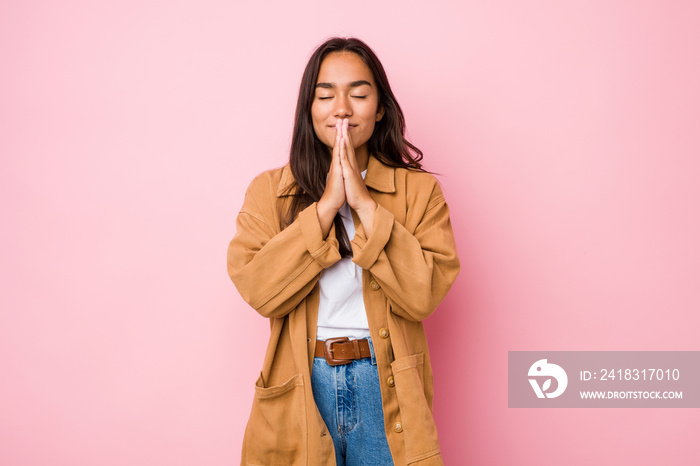 Young mixed race indian woman isolated holding hands in pray near mouth, feels confident.