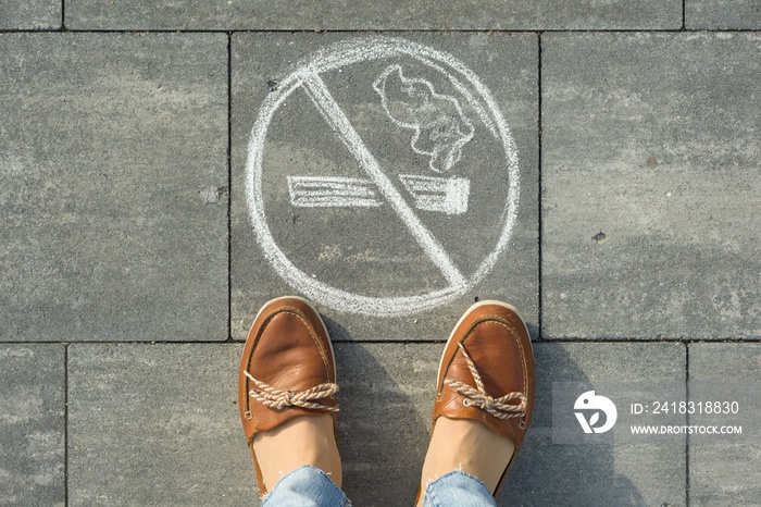 Female feet with picture no smoking painted on the grey sidewalk