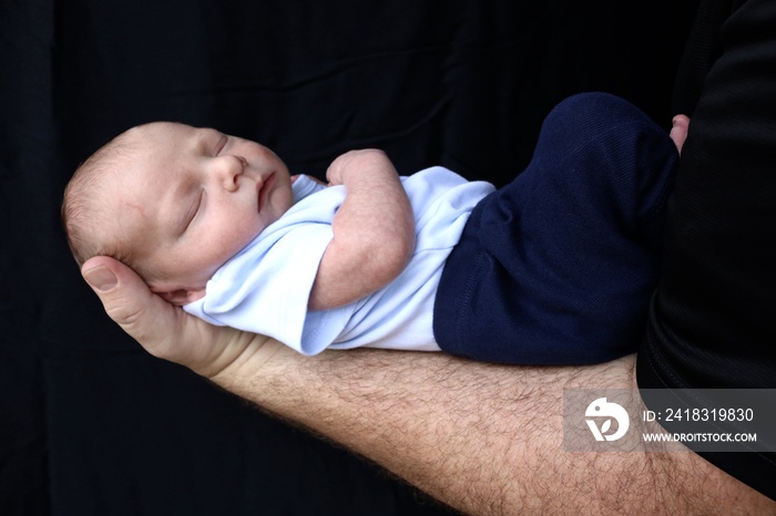 Newborn sleeping on his fathers arm against a black background