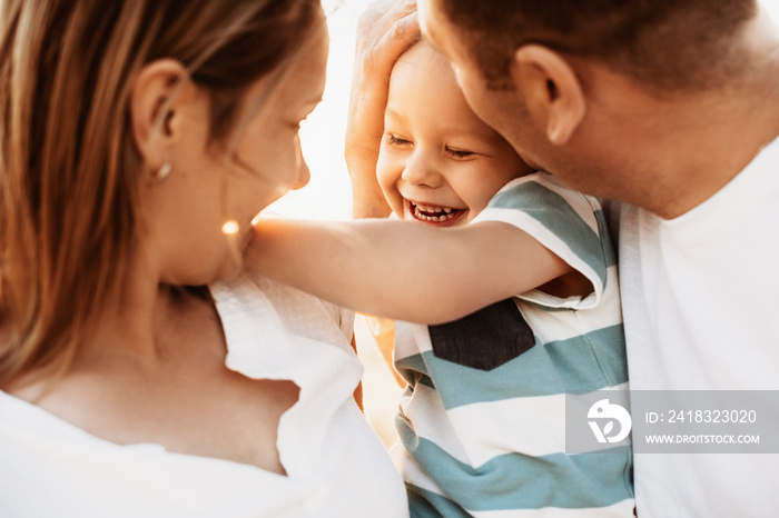 Close up portrait of mother and father kissing their son while embracing outside.