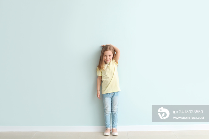 Cute little girl measuring her height near wall