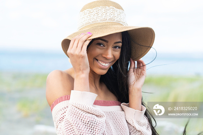 Pretty African American woman wearing floppy hat with a smile at the beach