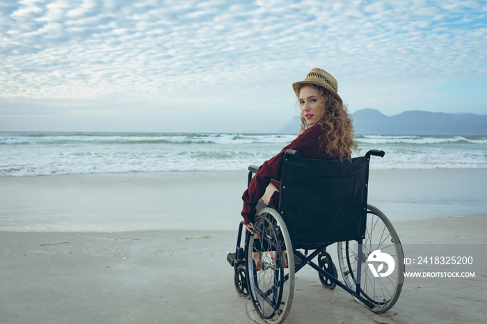 Disabled woman looking at camera sitting on wheelchair at beach