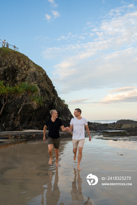 一对同性恋情侣手牵着手在海滩上奔跑，树和石头互相看着对方，傻笑
