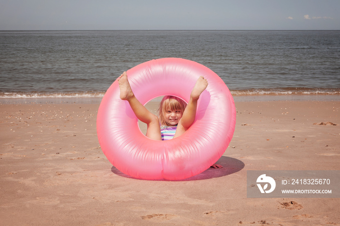 Girl (4-5) in inflatable ring on beach