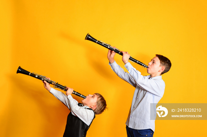 两个孩子在黄色背景上吹单簧管