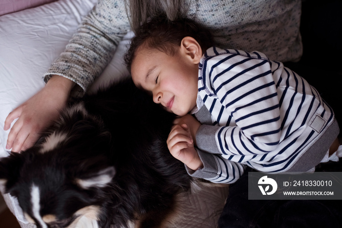 Midsection of mother sitting by cute son and dog sleeping on bed at home