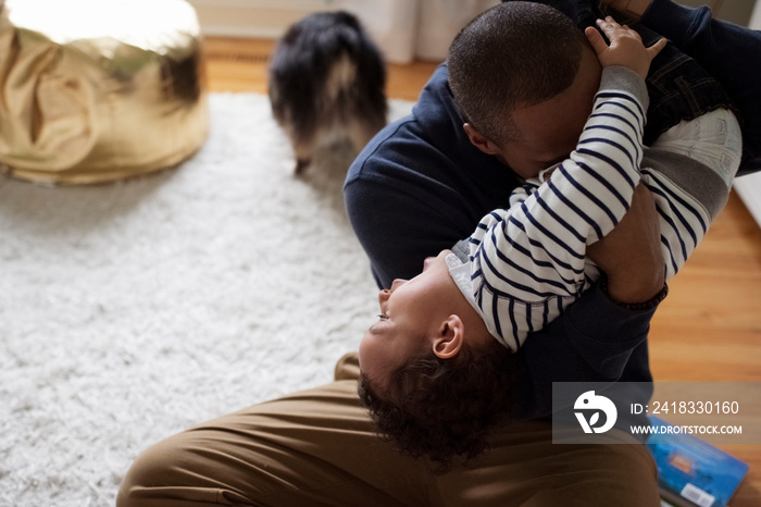 Playful father carrying happy son upside down while sitting on rug at home