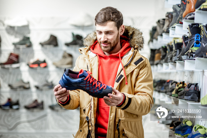 Man in winter jacket choosing trail shoes for mountain hiking in the sports shop