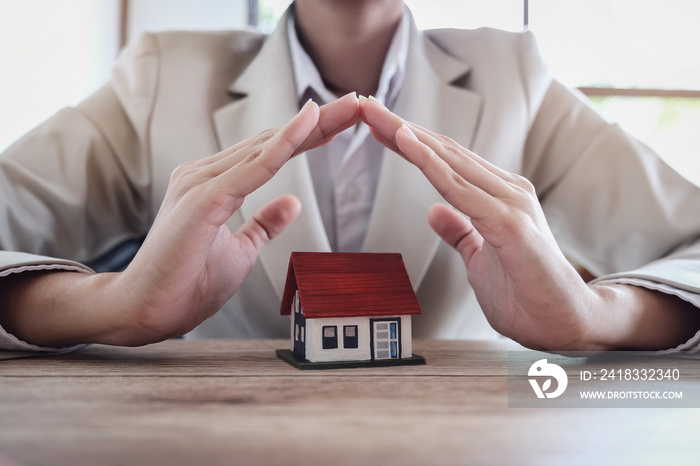 Insurance concept, woman hand protecting a house under his hands...