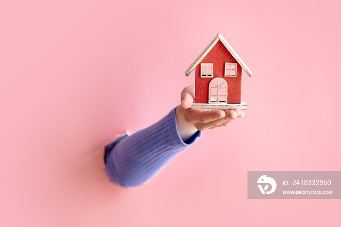 female hand hold little toy house on pink background.