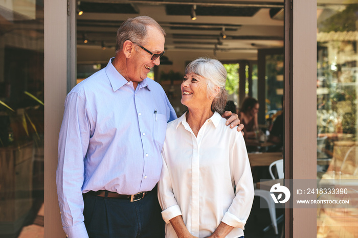 Senior couple standing at the entrance of their cafe