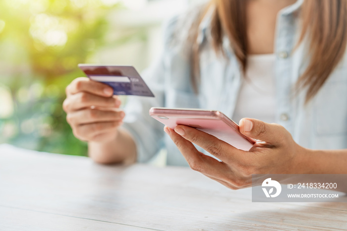 Young woman holding a credit card and using smartphone for making online payment shopping