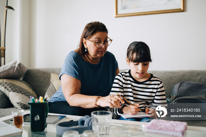 Grandmother assisting girl in homework on sofa at home