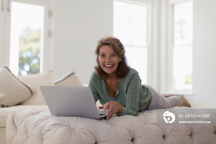 Portrait happy senior woman using laptop on ottoman