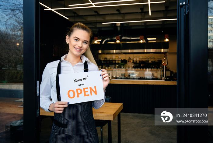 Woman welcoming customers at restaurant entrance with open sign - small business restaurant