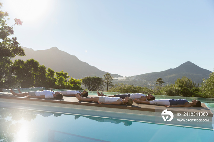 Yoga class practicing corpse pose at sunny poolside