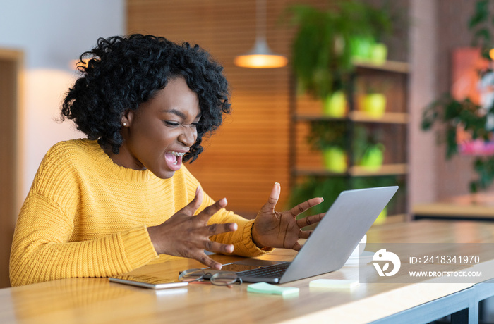 Angry black businesswoman screaming at laptop screen