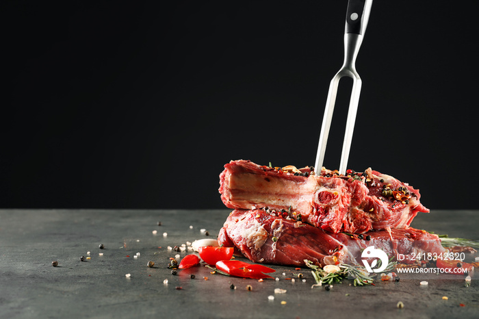 Composition with meat fork and raw steaks on table against black background