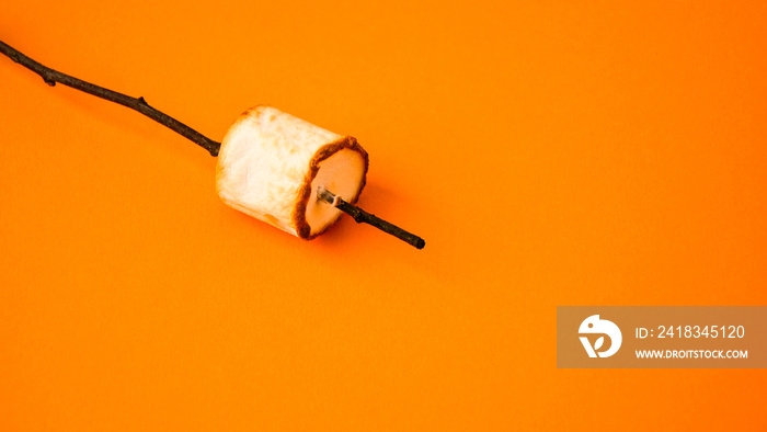 Grilled marshmallow on stick on yellow background with copy space. Fall camping fun