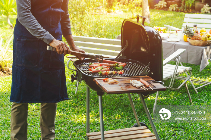 Handsome man preparing barbecue for friends in the garden.- Image