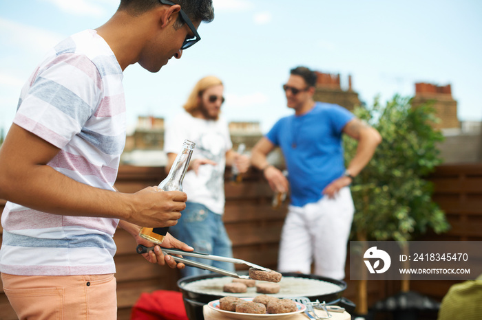 Young man barbecuing burgers at rooftop barbecue