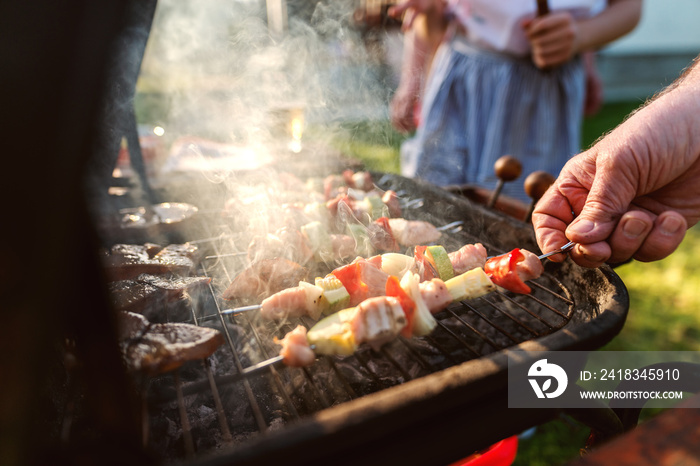 Close up of grandfather checking grilled meat and vegetables on stick while standing in backyard.