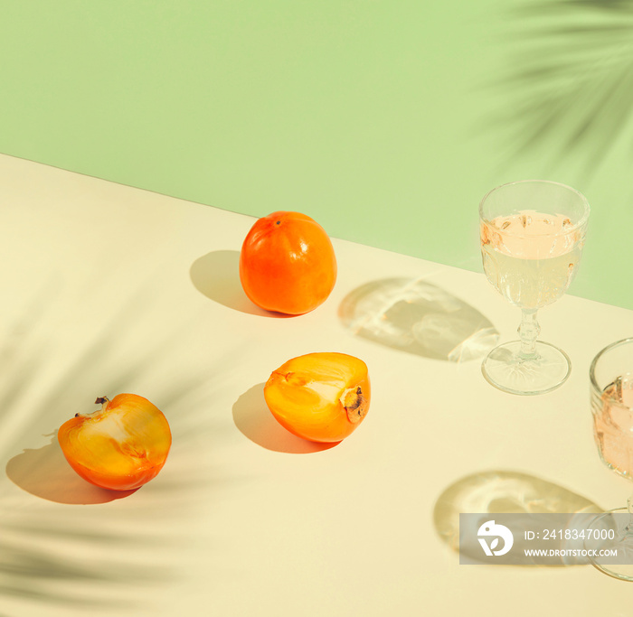 几何柔和背景上的柿子果实和玻璃杯，带有阳光和棕榈树叶子