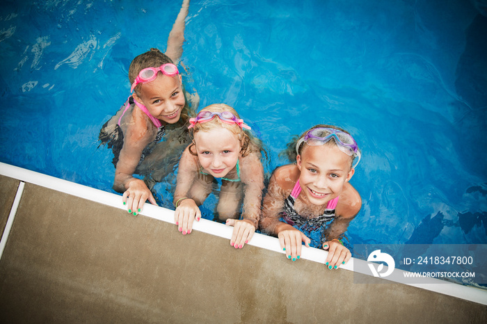 Elevated view of girls (8-9) with swimming goggles in swimming pool hanging by wall and looking up