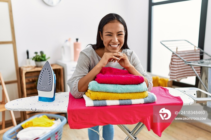 Young latin woman smiling confident leaning on iron board at laundry room