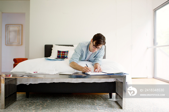 Young man lying on bed and writing in notebook