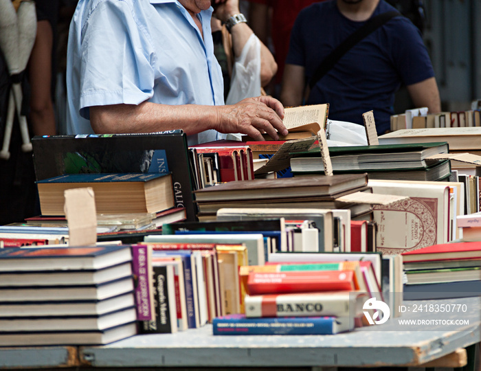 Anciano viendo libros en puesto callejero.