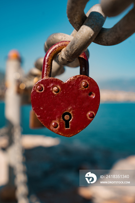 Red heart padlock on chain in front of blue sea and lighthouse, symbol of eternal love