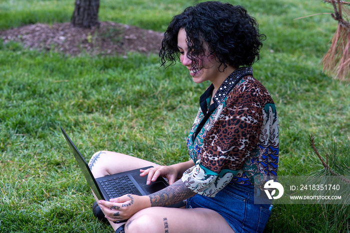 Smiling woman using laptop on lawn�in park