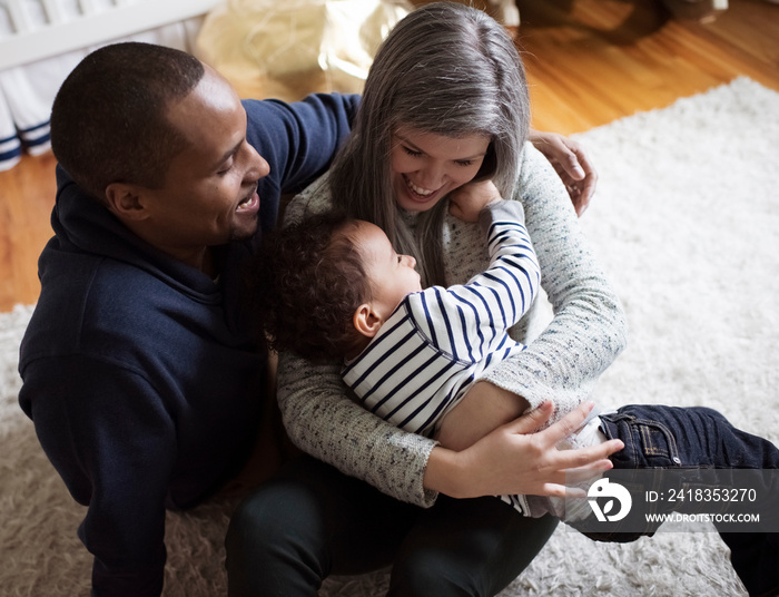 High angle view of happy father sitting by mother holding son while sitting on rug at home