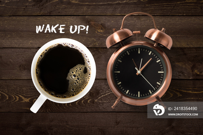 Mug of coffee and classical copper colored alarm clock with bells in a Wake Up concept on a wooden t