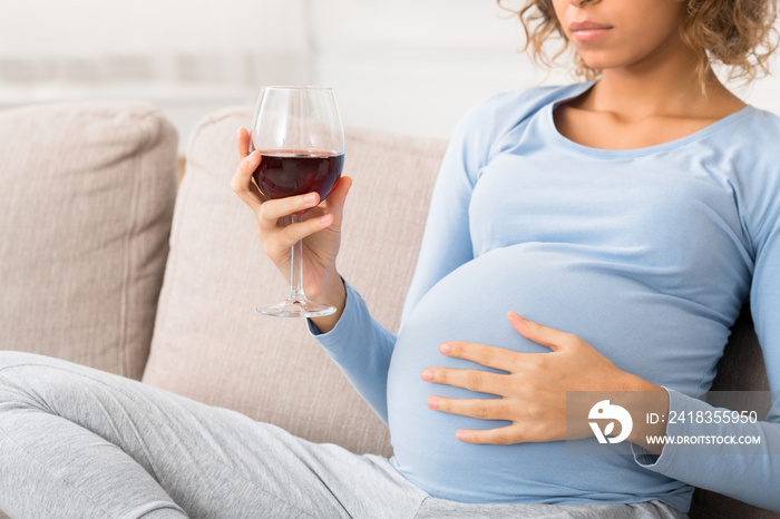 Irresponsible expectant woman holding glass of wine