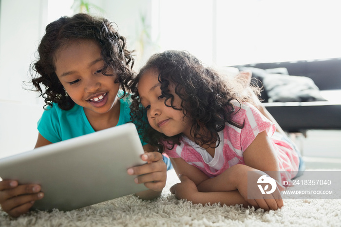 Sisters using digital tablet while lying on rug in living room