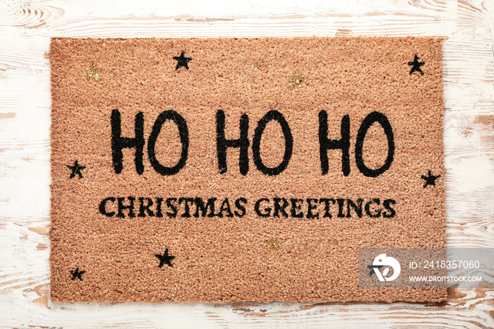 Door mat with Christmas greeting on wooden background