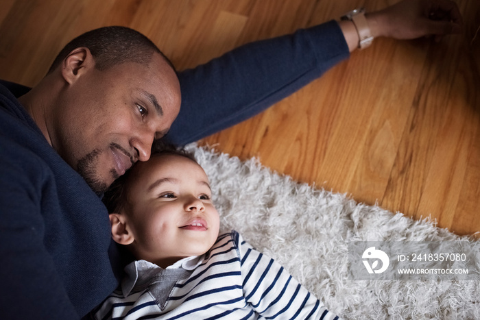 High angle view of thoughtful father and cute son looking away while relaxing on rug at home