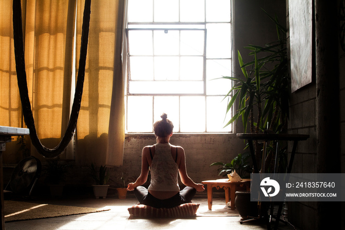 Rear view of woman meditating in living room