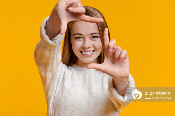 Smiling girl framing face with fingers, pretending to capture photo