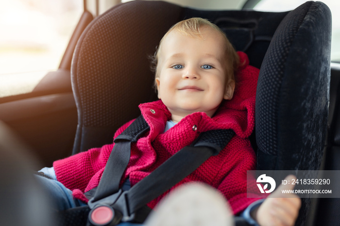 可爱的高加索嘟嘟男孩在公路旅行中坐在车里的儿童安全座椅上。可爱的婴儿微笑