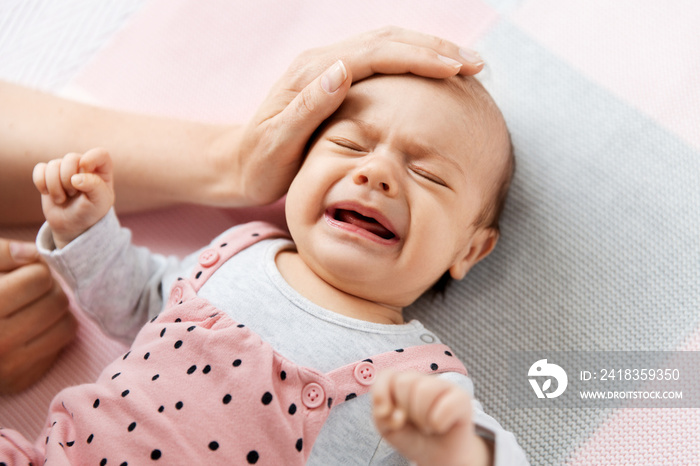 babyhood, motherhood and people concept - mothers hand touching crying little baby daughter lying o