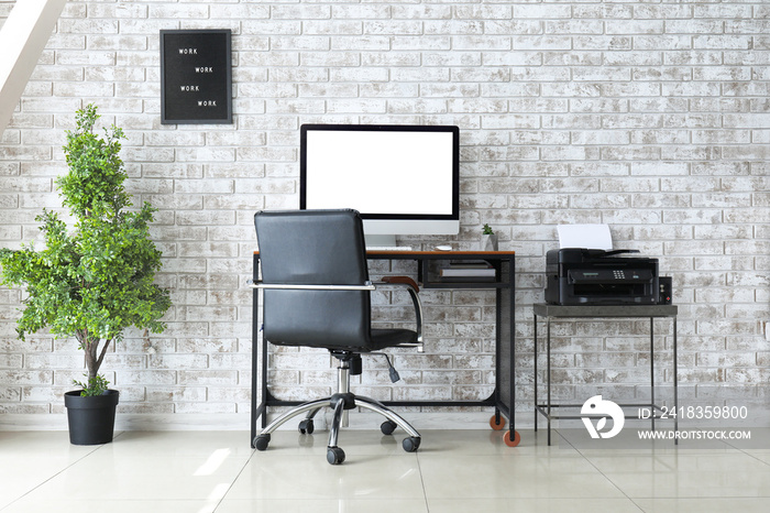 Interior of room with comfortable workplace near brick wall