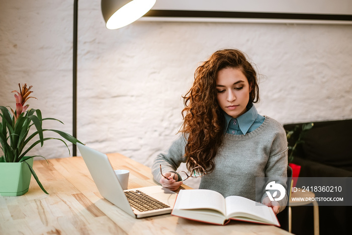 Woman reading book while sitting by the desk.